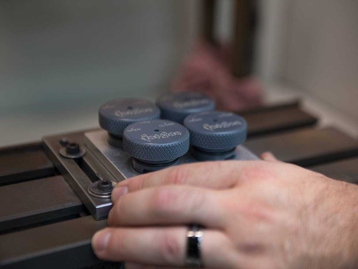 A hand adjusts knobs on a metal apparatus with engraved text.