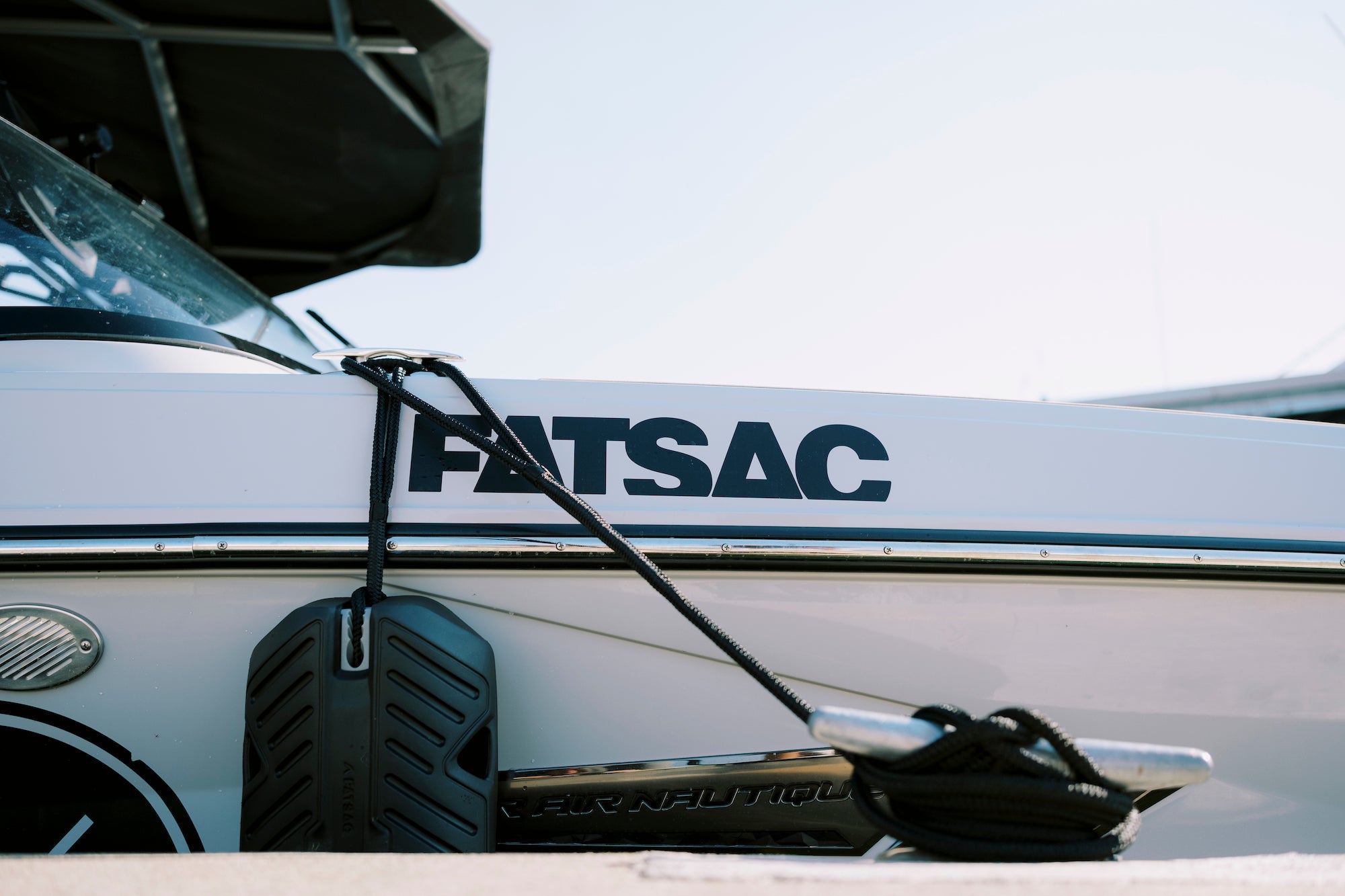 Close-up of a boat with FATSAC written on the side, featuring a black rope and fender.
