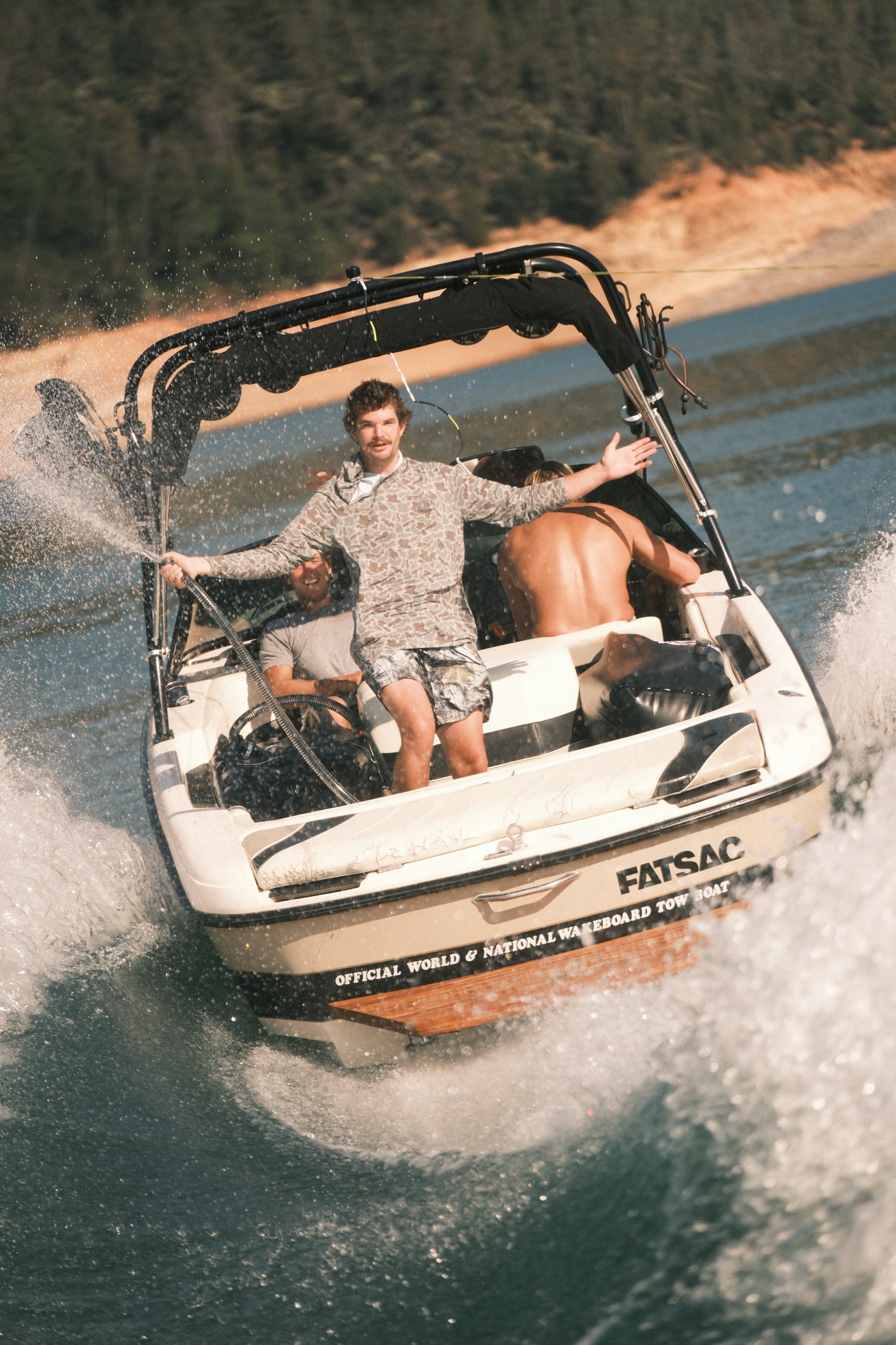 Three people on a boat with 'FATSAC' branding, speeding through water while one is spraying water in the air from a hose.