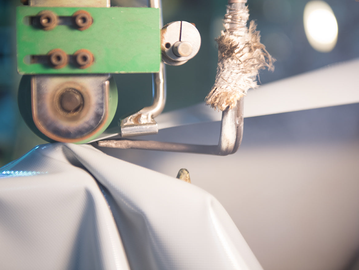 Close-up of a machine seaming white fabric with a green apparatus and a heated element.