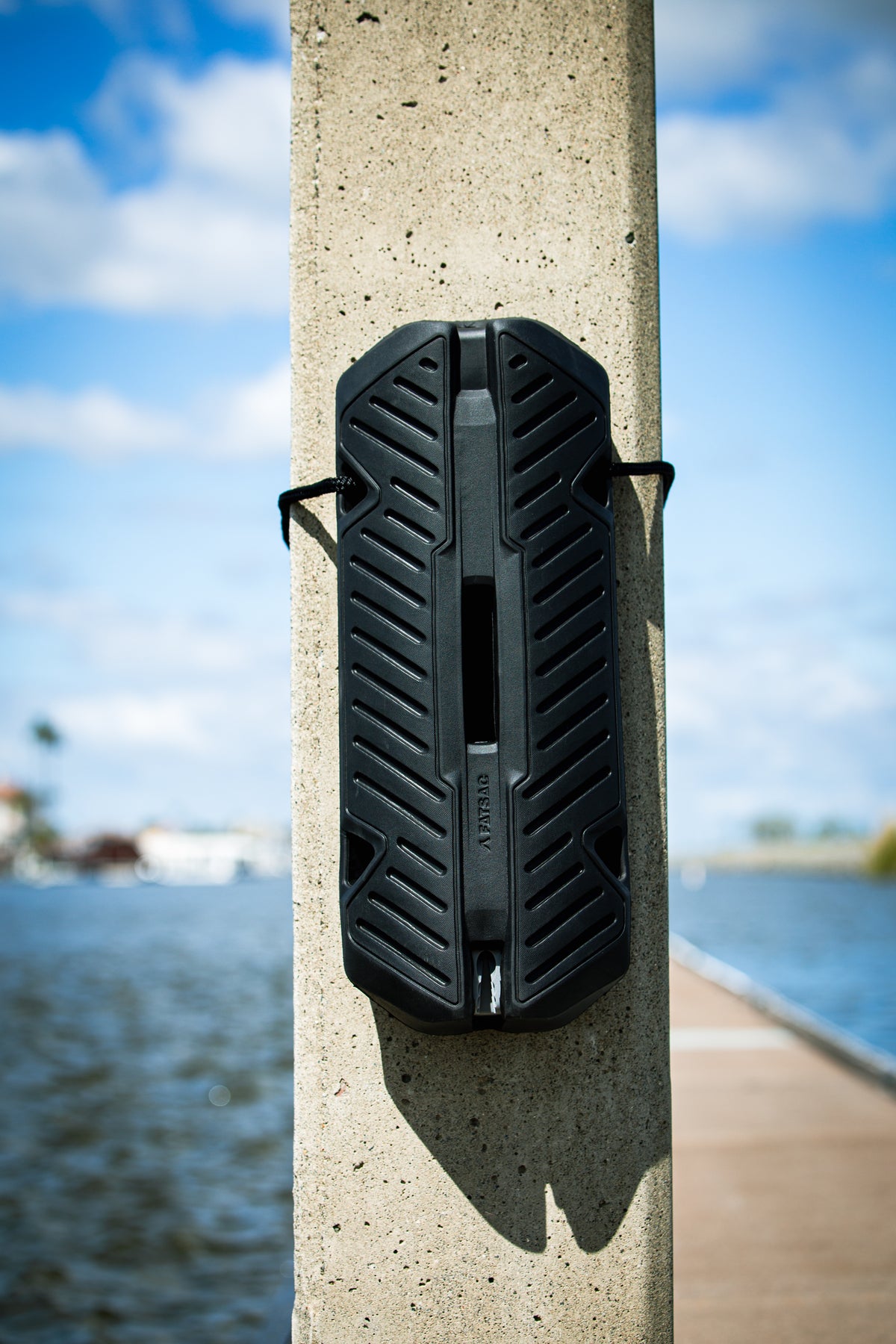 Fatsac black fender with dock line attached to a concrete pillar by the waterfront.
