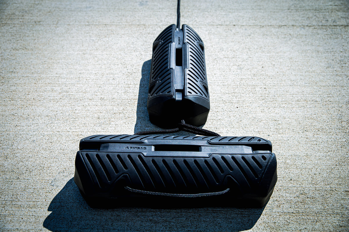 Fatsac black boat fender with straps on a concrete dock.