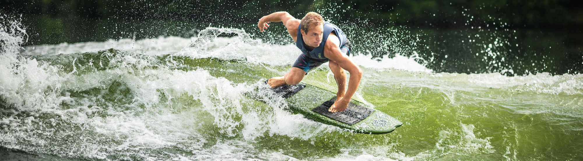 Wakesurfer in a blue vest carves through a breaking wake with water spraying around.