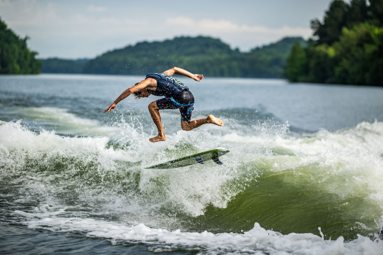 Wakesurfer mid-flip above the wake, board rotated and water splashing beneath.